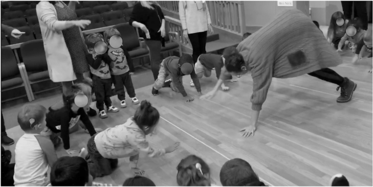 A woman and a cirlce of children are on all fours role-playing as animals.