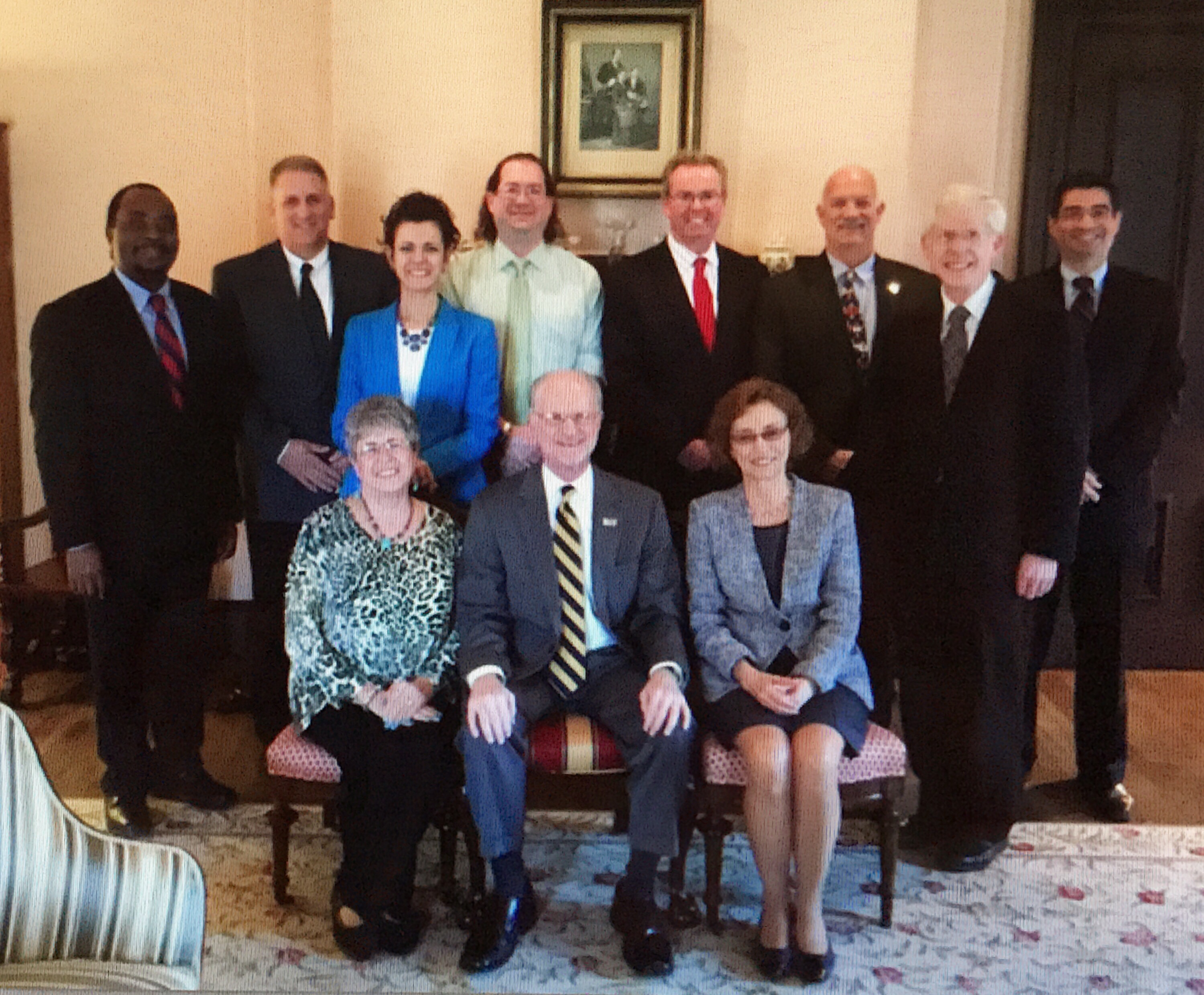 A group of eleven middle-aged to older adults in a room. There are three white women and one Black man. All the rest are white men.