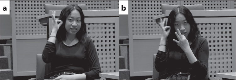 Hyemi, a young Korean woman with shoulder-length black hair, is signing two variants of HEARING. a) Her right hand is raised to her right ear, palm inwards, index finger and thumb touching, rest of her fingers splayed. b) Both hands are raised. Her right hand is raised to her right ear, palm inwards, index finger and thumb touching, rest of her fingers splayed. Her left hand is raised to chin level, palm facing inwards, index finger and thumb touching, rest of her fingers splayed.