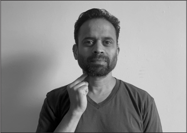 Sujit, an Indian man with a short black beard, signs THIRUVANANTHAPURAM (right hand closed at neck, index and middle finger extended together touching neck).