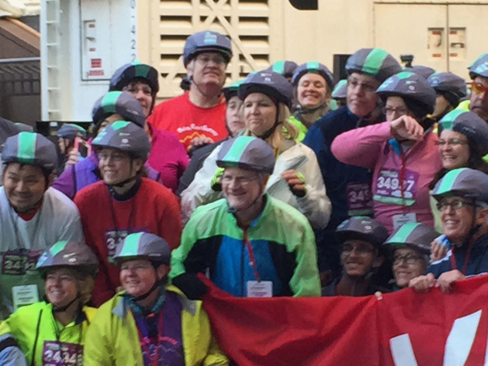 A group of bicyclists pose for a photo on a street in New York City. All of their helmets are black with a green stripe down the middle.