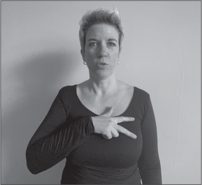 Annelies, a white woman with short blonde hair, signs SOZIAL (right hand palm down over left pec; thumb, index and middle fingers extended and splayed).