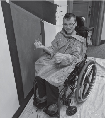A young boy in a wheelchair paints a mural.