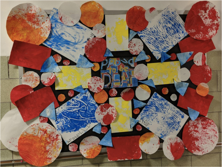 Bulletin board filled with circles and rectangles painted either red, blue, or yellow. In the center are the words “Proud to be Deaf”