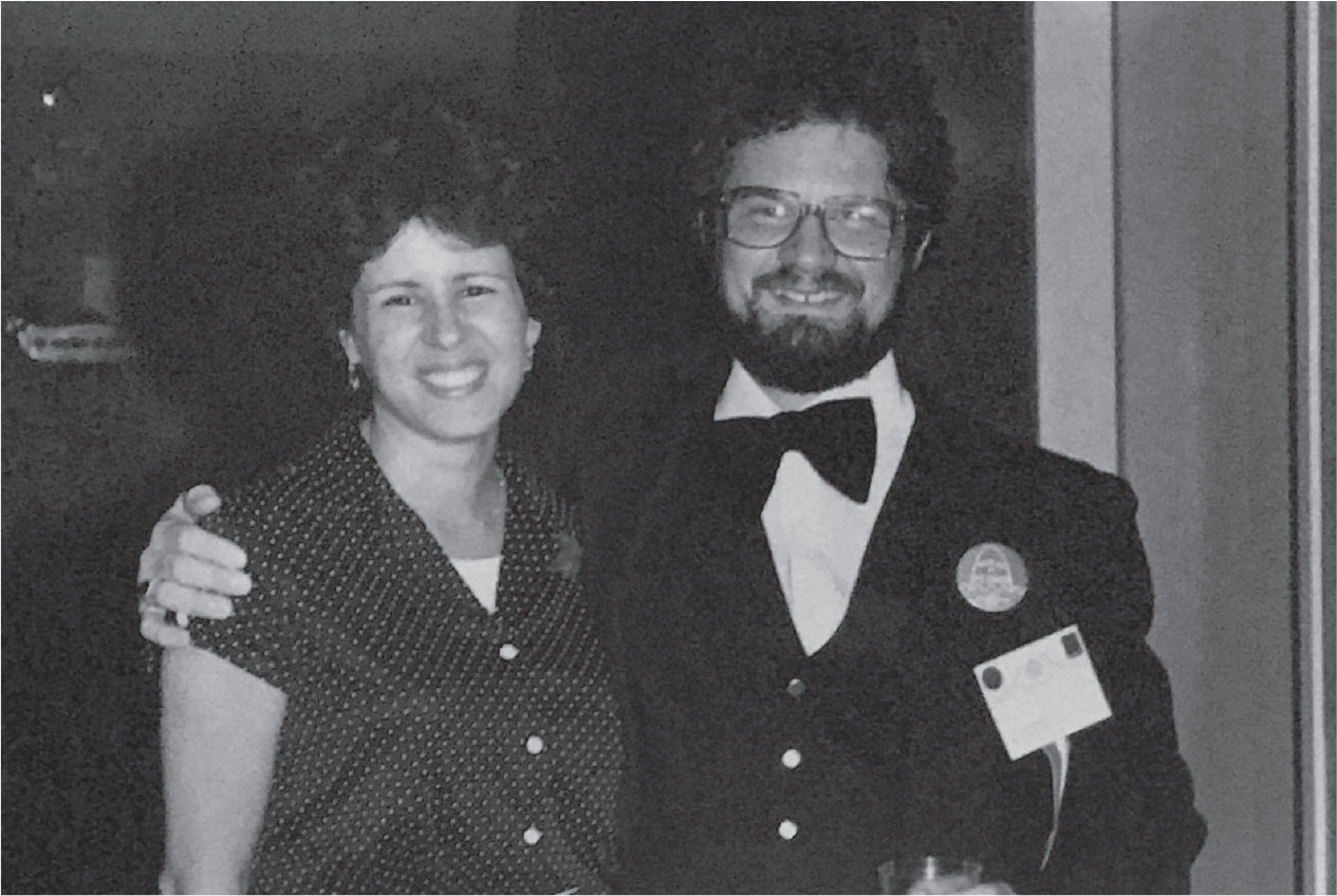 A black-and-white photo of a young white woman in a polka dot blouse with a young white man with glasses and a mustache and beard. he's wearing a bow tie and has his arm around the woman.