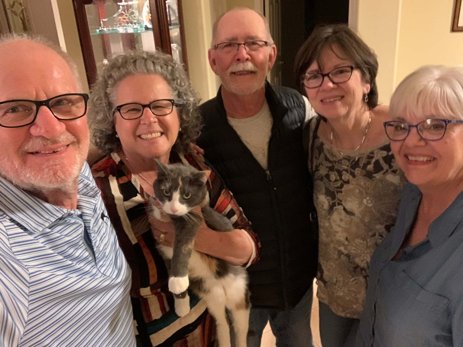 A group of older white adults looking up into a camera. One woman is holding a gray and white cat.