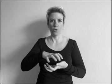 Annelies, a white woman with short blonde hair, signs ROME (both hands clawed, right hand over left, palms facing each other).